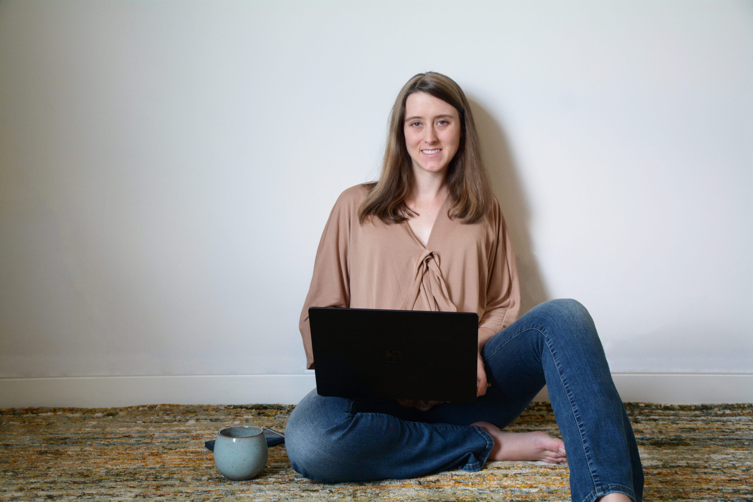 Caitlyn, owner of Upwell Strategies sitting on the floor with her laptop on her lap.