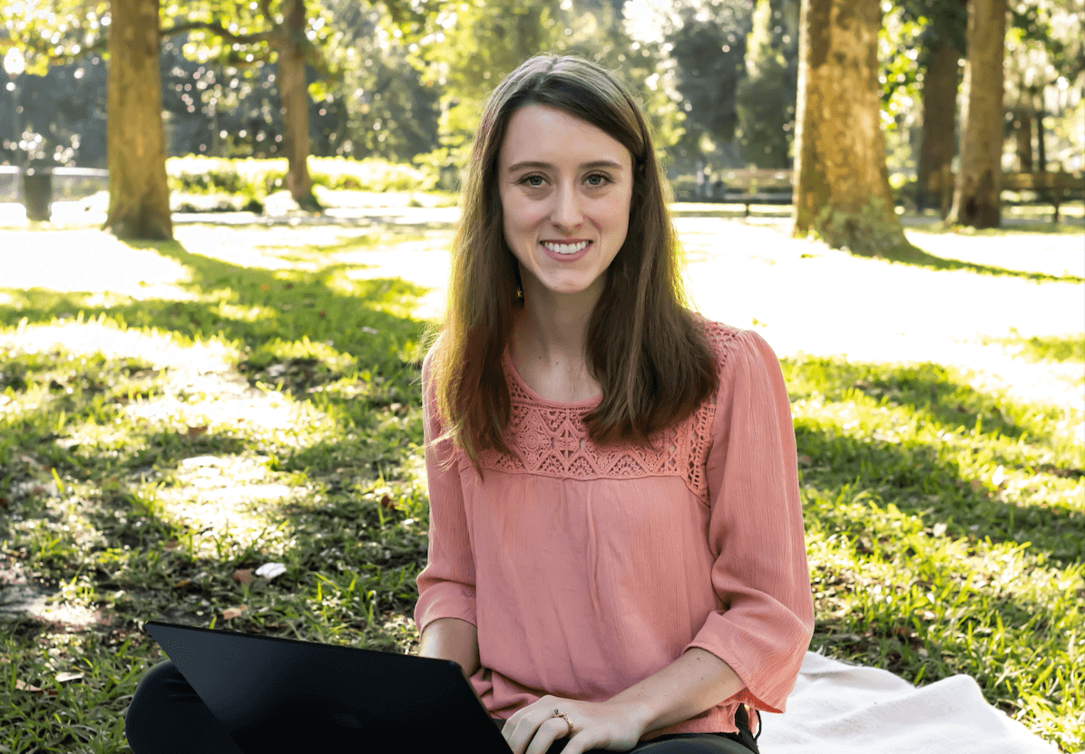 Caitlyn Wells of Upwell Strategies is on laptop computer in a park with green grass and trees in background